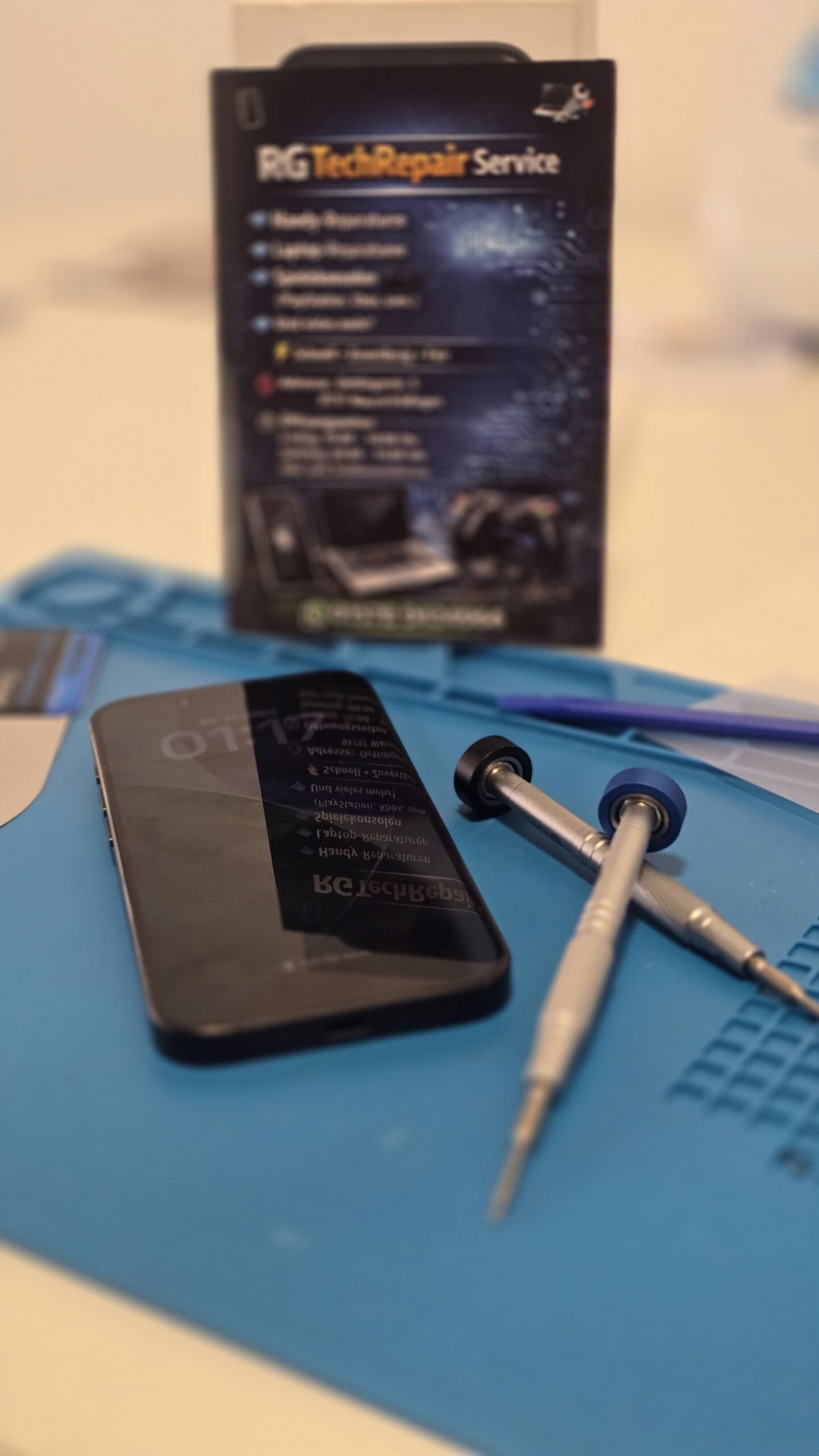 Smartphone auf einer blauen Reparaturmatte mit Präzisionswerkzeug beim RG TechRepair Service